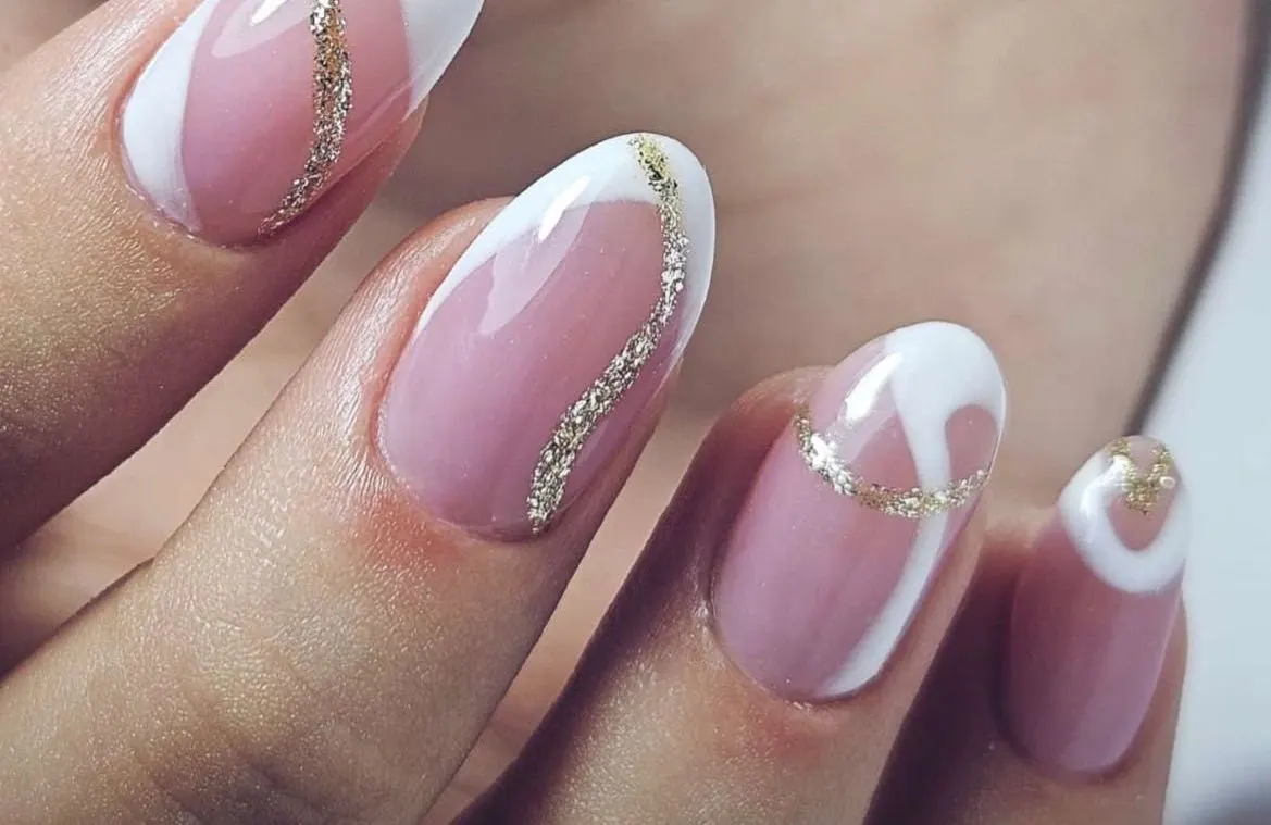 Uñas ovaladas rosadas con puntas blancas y una línea ondulada de brillo dorado.